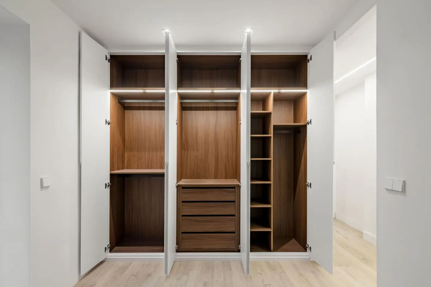Modern walk-in closet with white doors, warm wood interior, built-in drawers, shelving, and integrated LED lighting.
