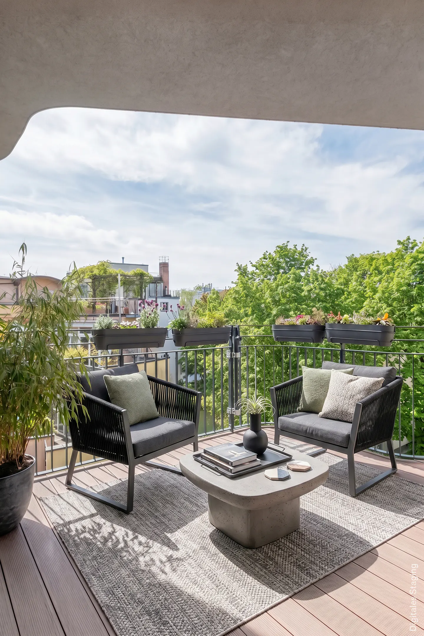 Outdoor patio with two gray sofas, a concrete coffee table, and a gray rug. Balcony overlooks trees and buildings.