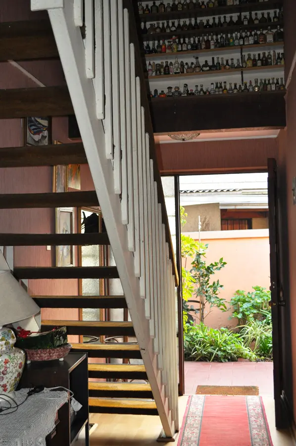 Interior view of a home with wooden stairs and white railings, leading to a doorway with a view of a garden. Shelves above the door are filled with small decorative items.