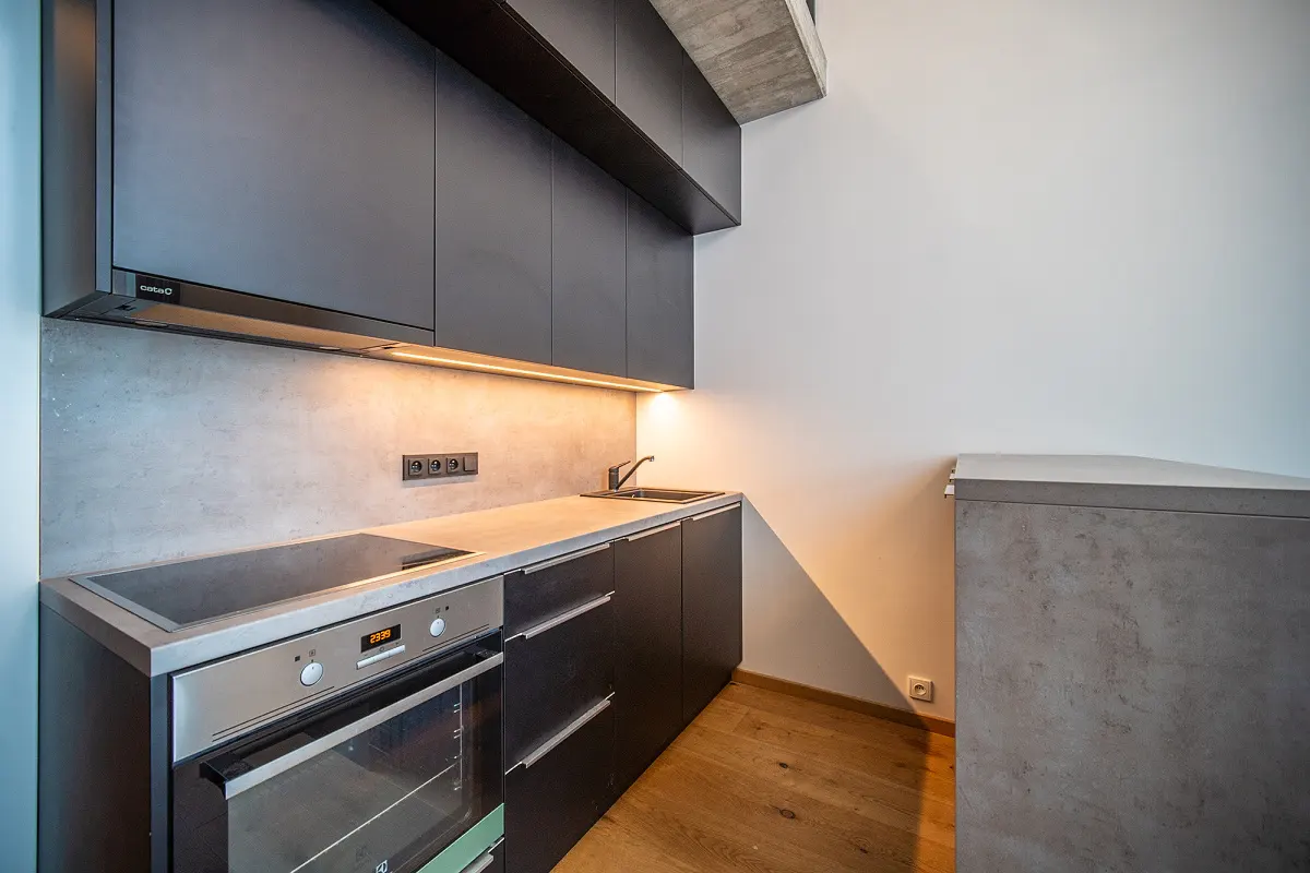 Modern kitchen with dark cabinets, concrete countertops and backsplash, stainless steel oven, and wood floors.