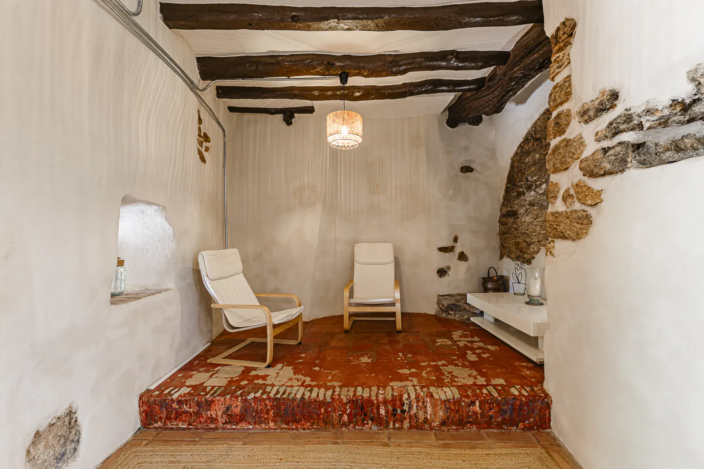 Rustic room with two chairs on a raised brick floor. Exposed beams on the ceiling and stone accents on the walls.