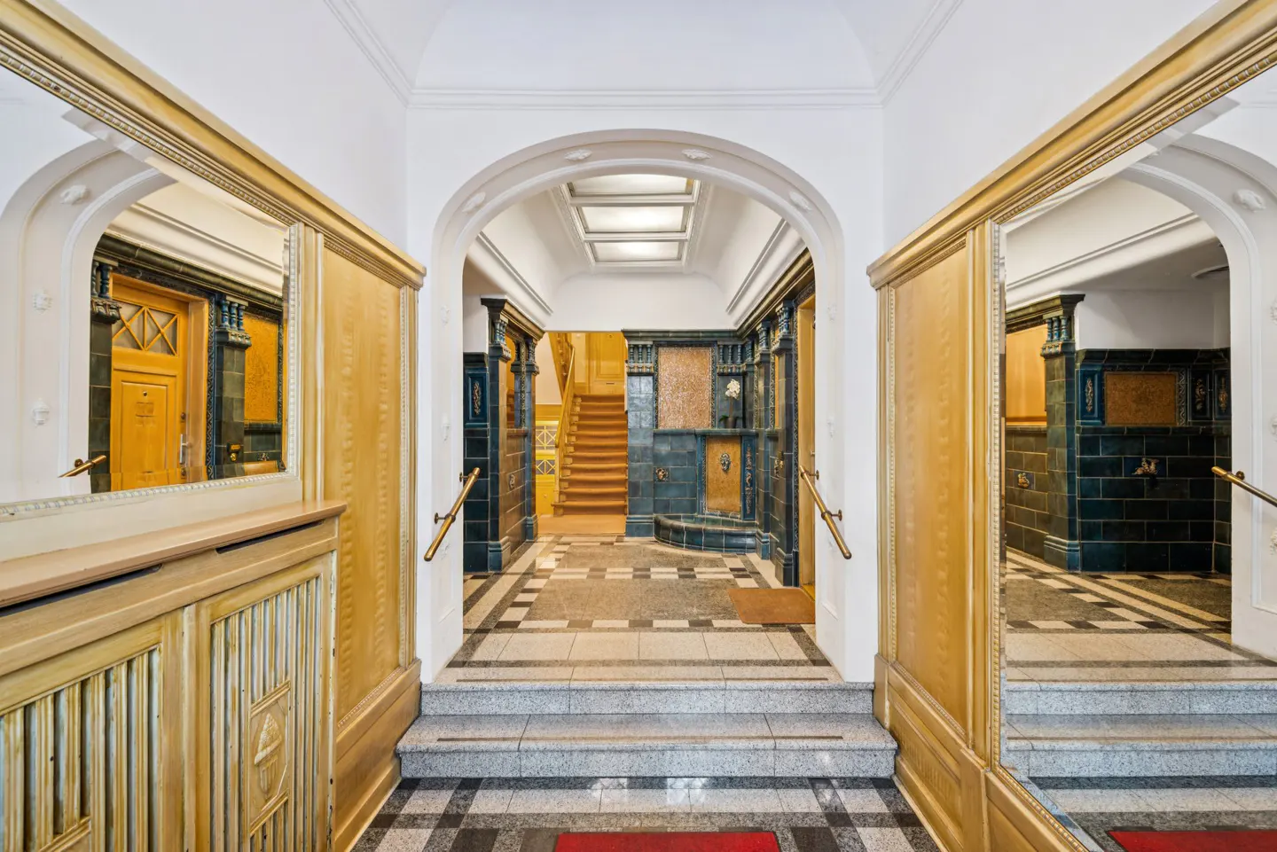 Ornate foyer with arched doorways, gold wood paneling, and tiled walls. A staircase is visible in the background.