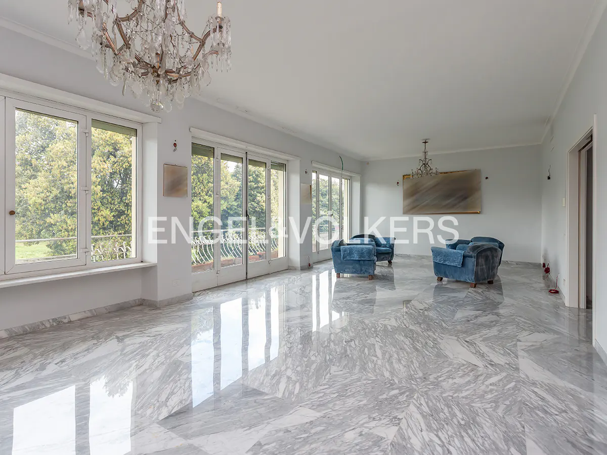 Bright, airy living room with marble floors, blue armchairs, and a chandelier. Windows overlook a green landscape.