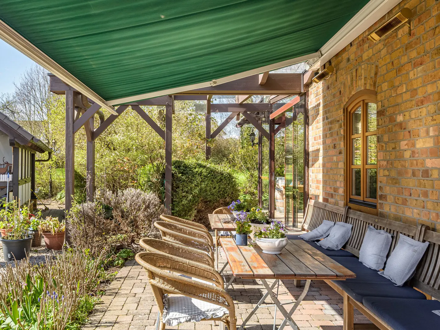 Outdoor patio with brick flooring, a wooden table and chairs, and a green awning. A brick building is on the right.