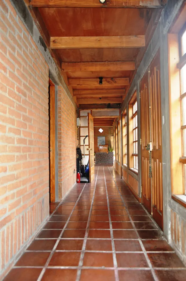 Hallway with brick walls, wood ceiling beams, and terracotta tile floor. Doors and windows line the right side.