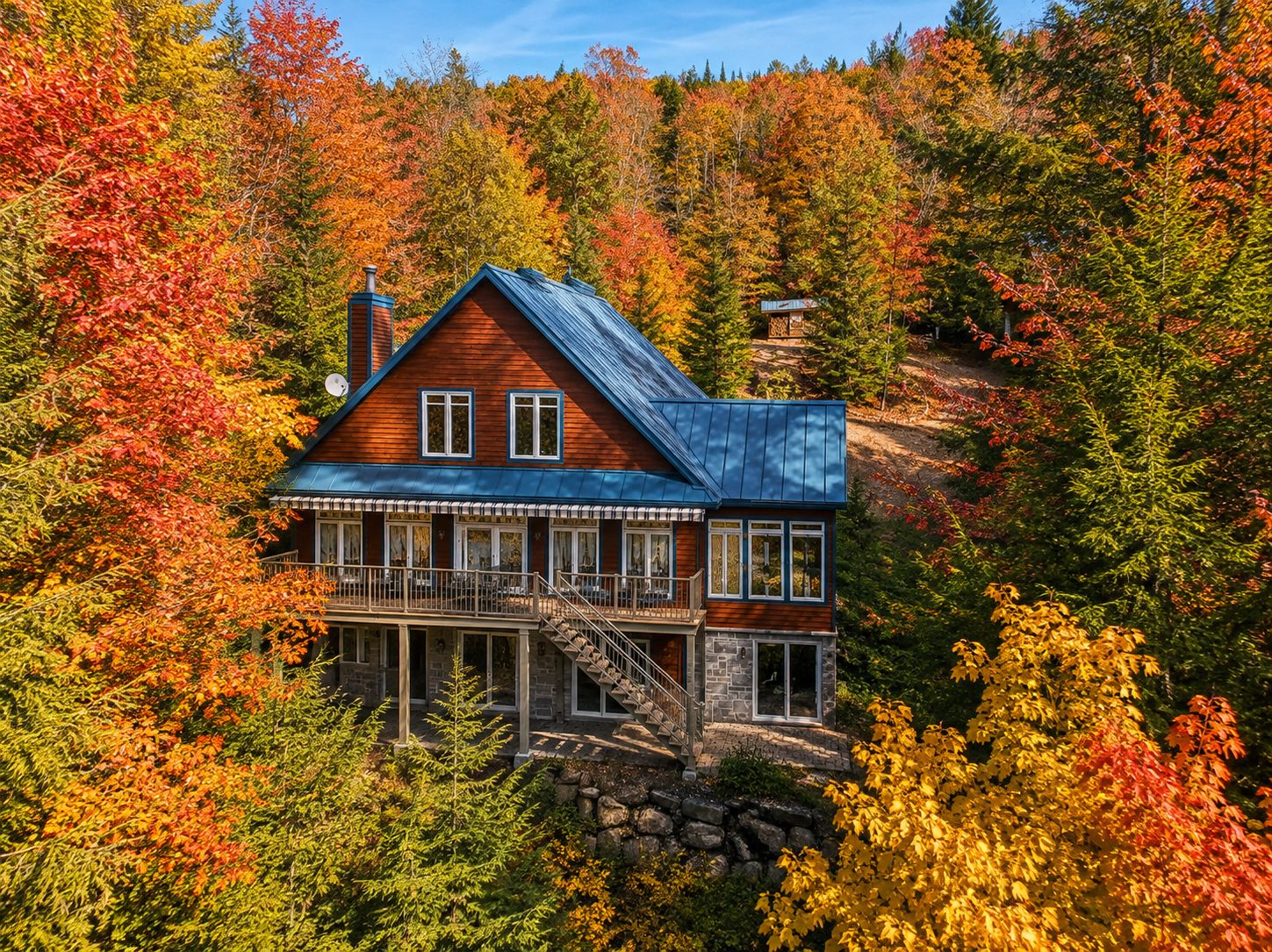 A two-story wooden cabin with a blue metal roof nestled in a forest of vibrant autumn trees with red and yellow leaves. [AI-generated text]