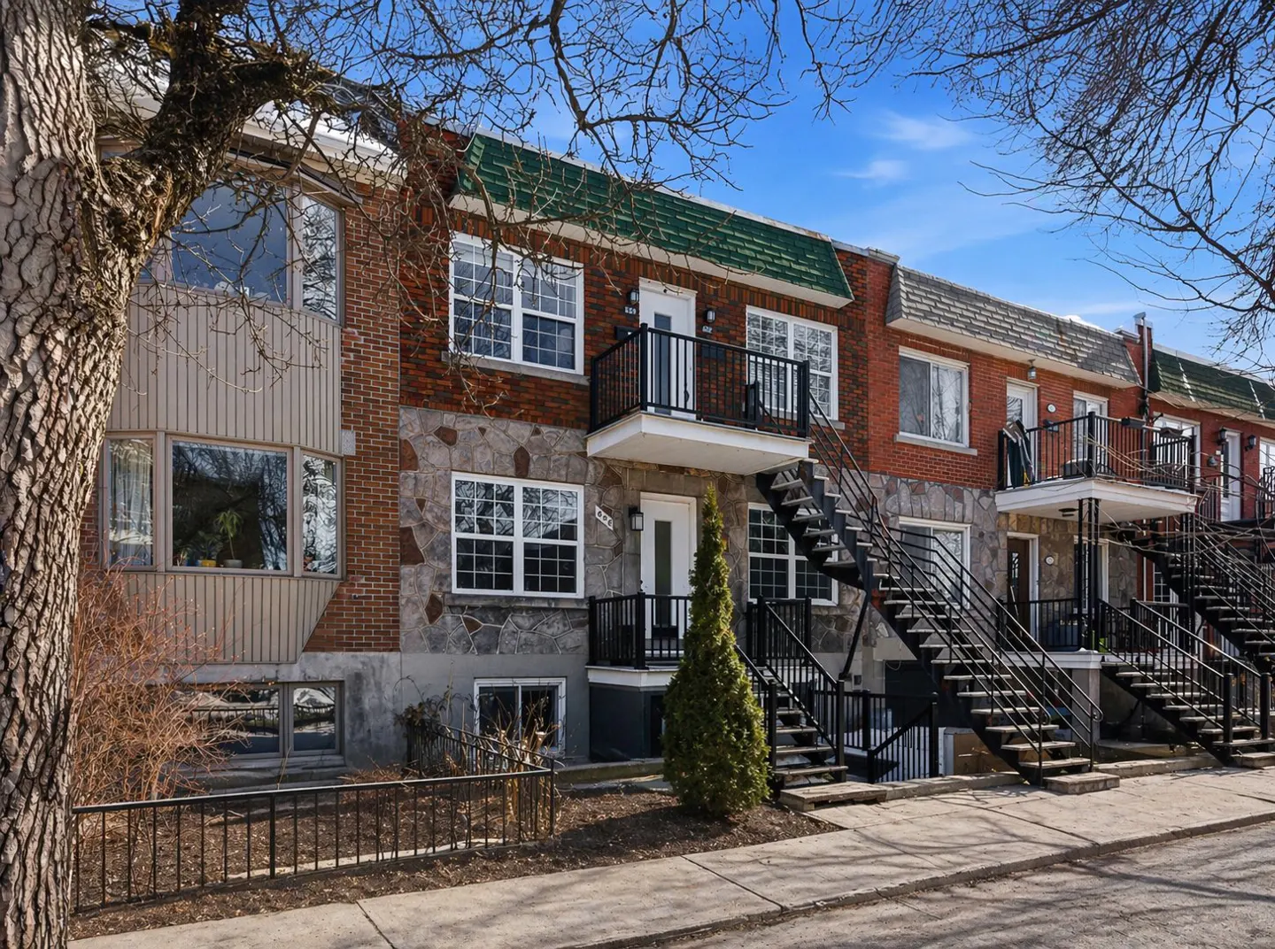 Row of brick and stone apartments with black metal stairs and balconies on a sunny day.