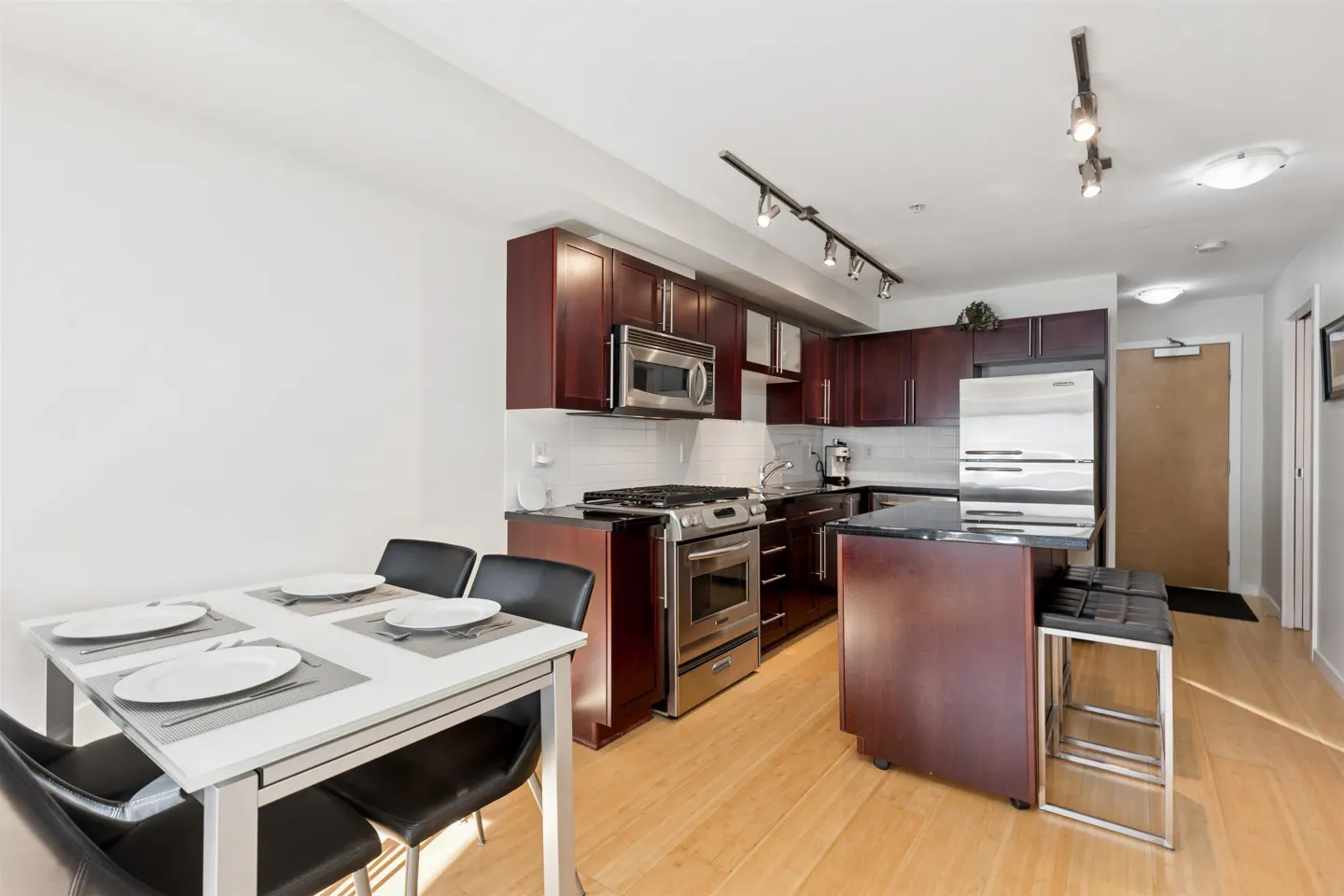 A modern kitchen with dark wood cabinets, stainless steel appliances, and a white dining table set for four.