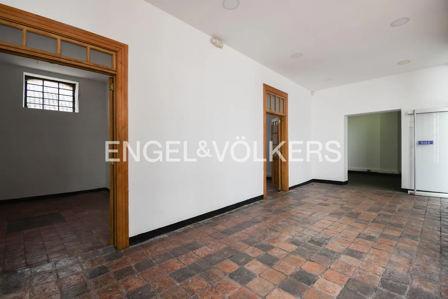 Empty room with white walls, terracotta tile floor, and wooden door frames. The Engel & Völkers logo is superimposed on the wall.