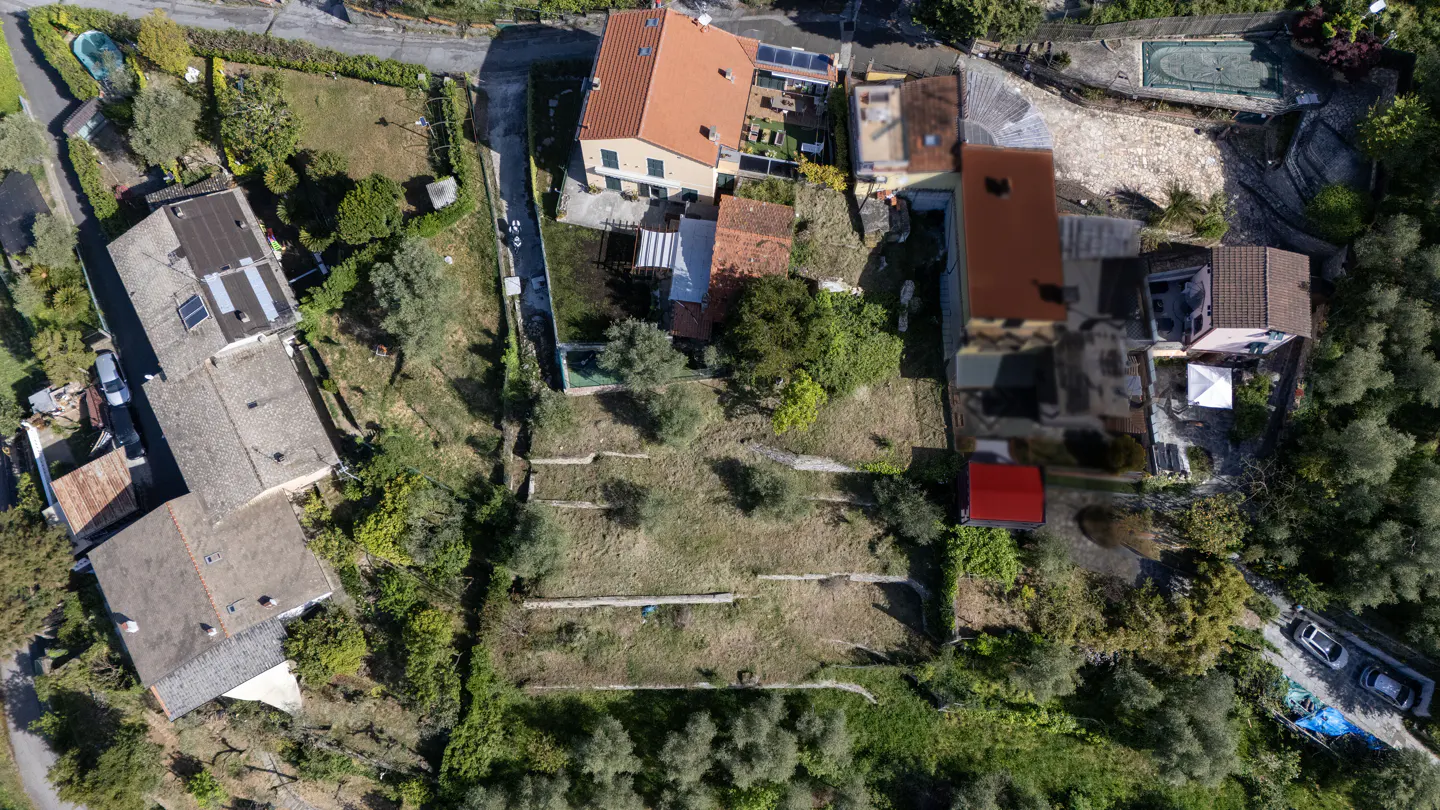 Aerial view of a property with a large, terraced lot, surrounded by houses and greenery.