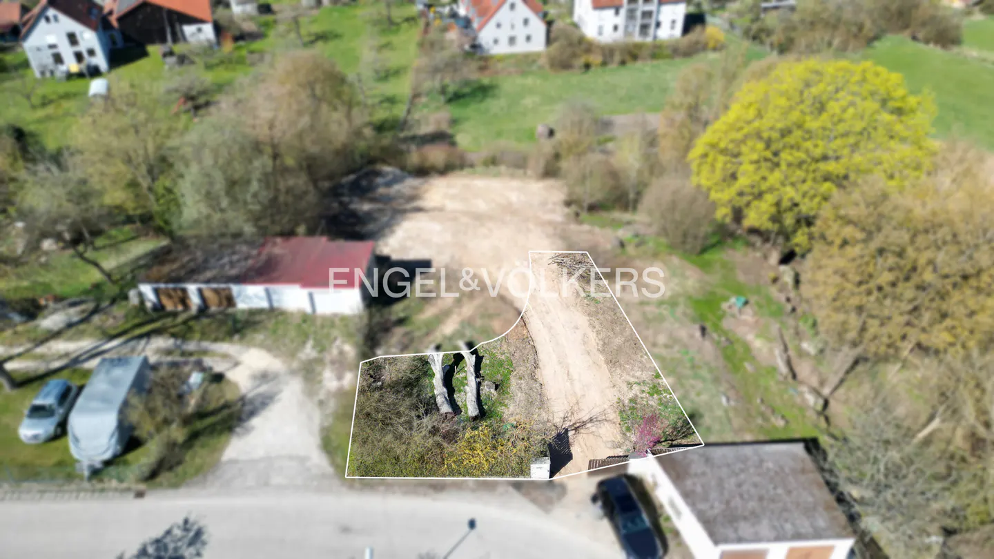 Aerial view of a vacant lot outlined in white, surrounded by trees and houses in a rural area. A dirt path runs through the center.