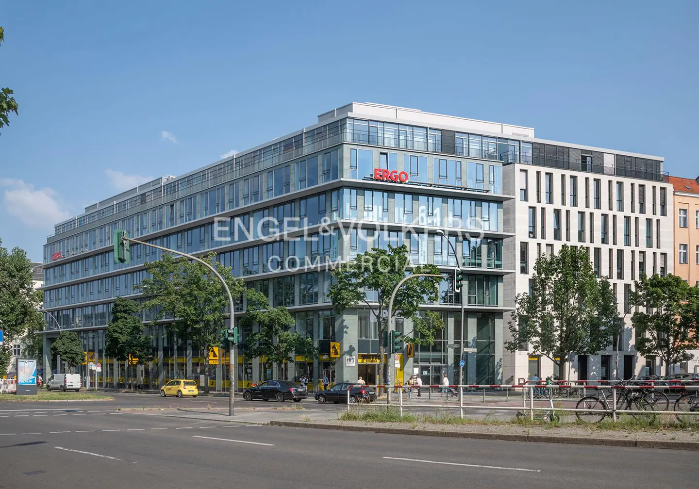 Exterior view of a modern, multi-story office building with glass facade and "ERGO" signage, street with cars and bikes.