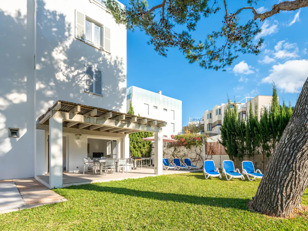 Exterior of a white house with a patio, lawn, and blue lounge chairs under a sunny sky.