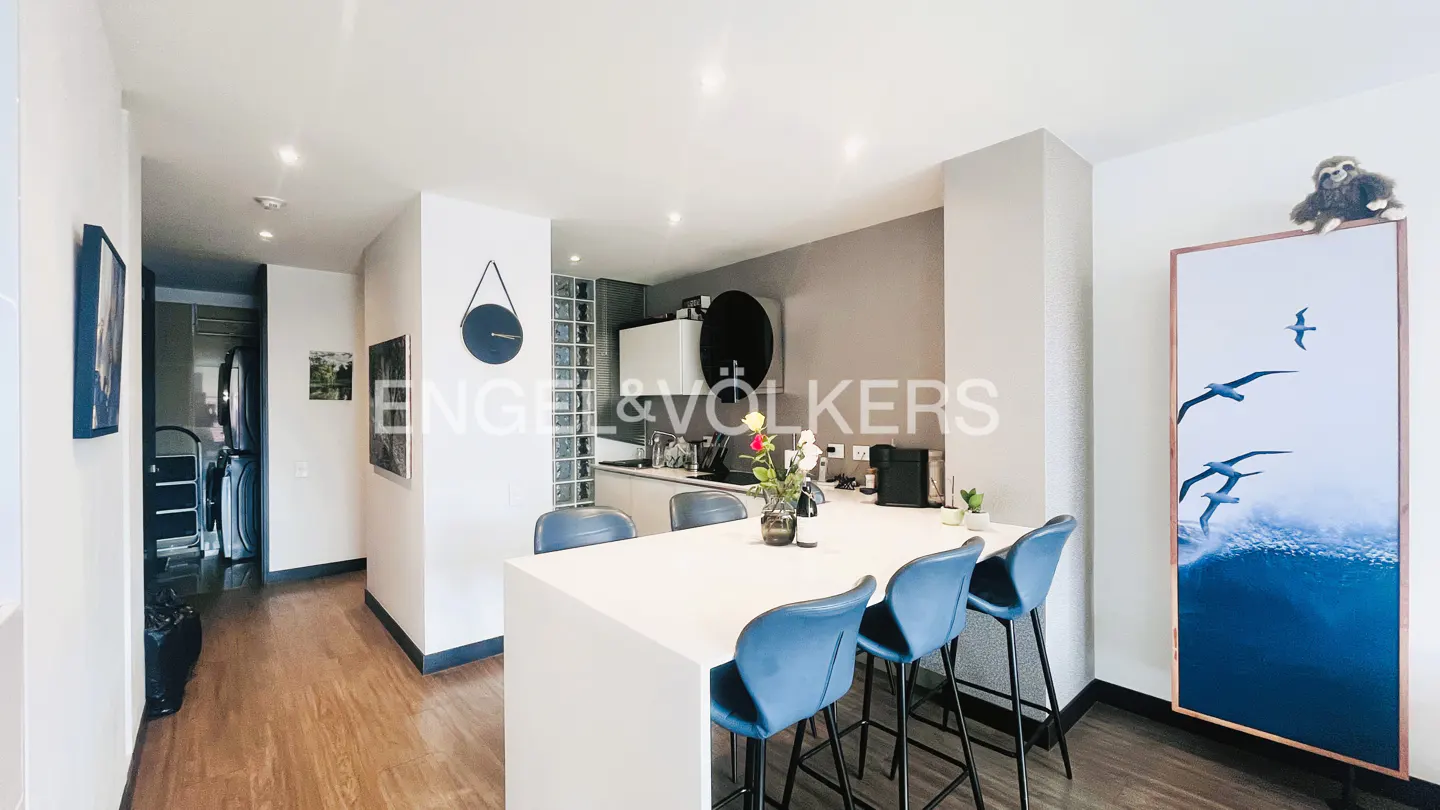 Modern kitchen with white island, four blue bar stools, and a tall artwork of seagulls over the ocean on the right.
