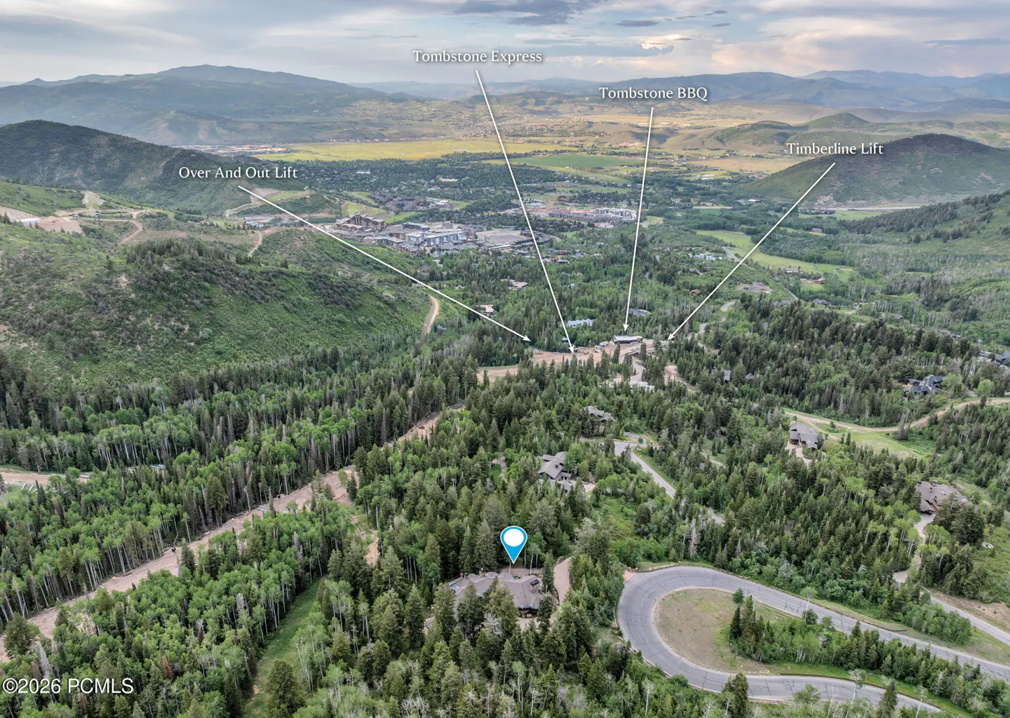 Aerial view of a house with a blue pin on top, surrounded by green trees and mountains in the background.