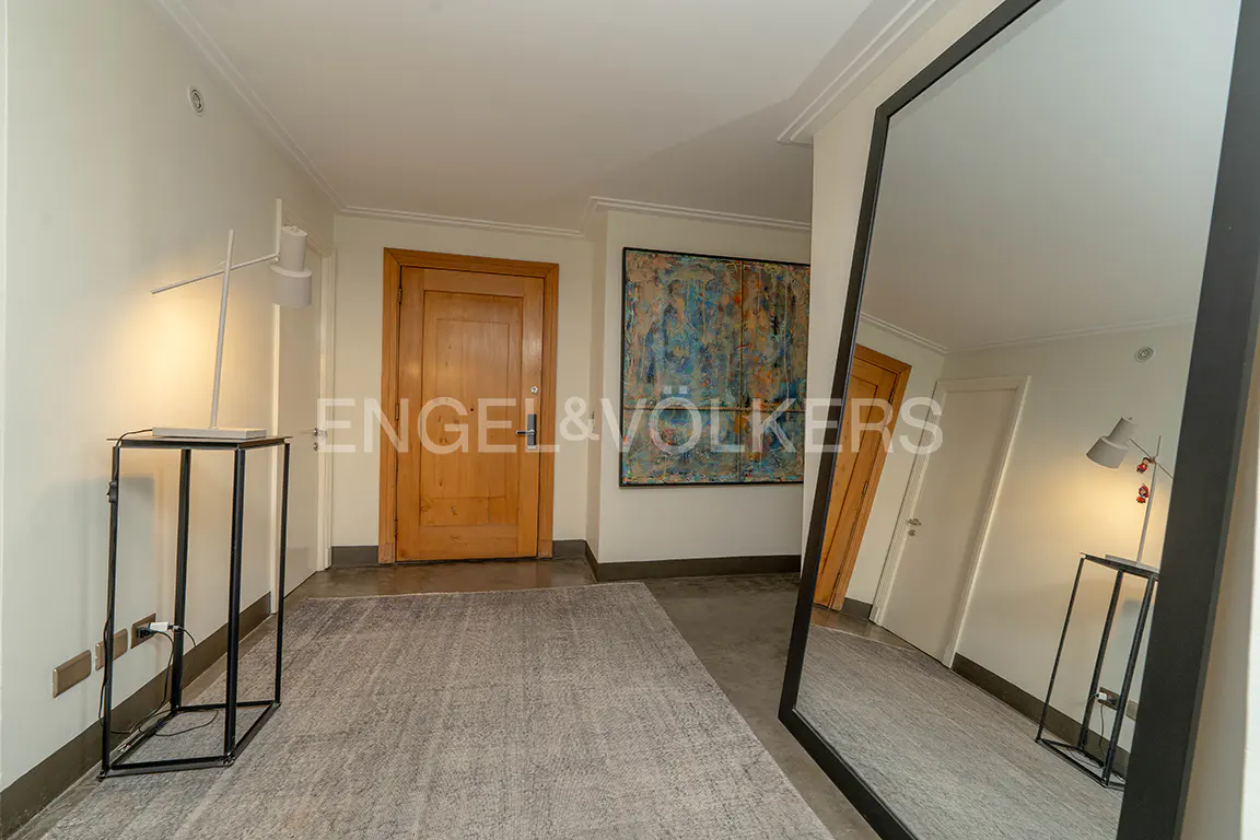 Modern hallway with a large floor mirror, grey area rug, wooden door, and abstract wall art.
