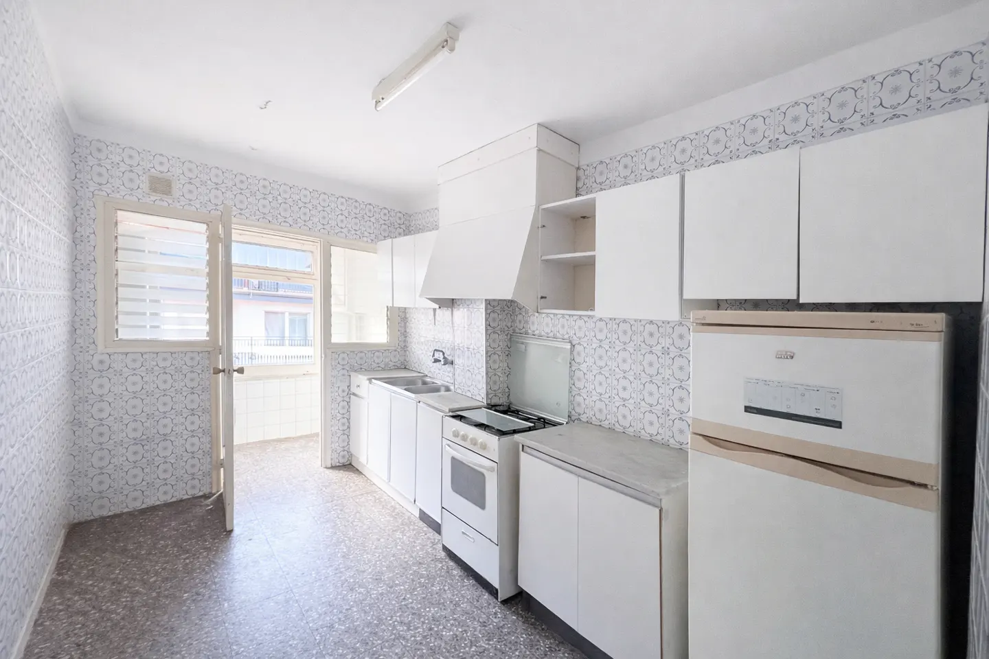Kitchen with white cabinets, a stove, and a refrigerator, featuring patterned wall tiles and a door leading to a balcony.