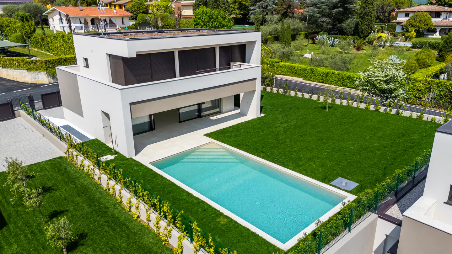 Aerial view of a modern, two-story white house with a rectangular swimming pool and green lawn.
