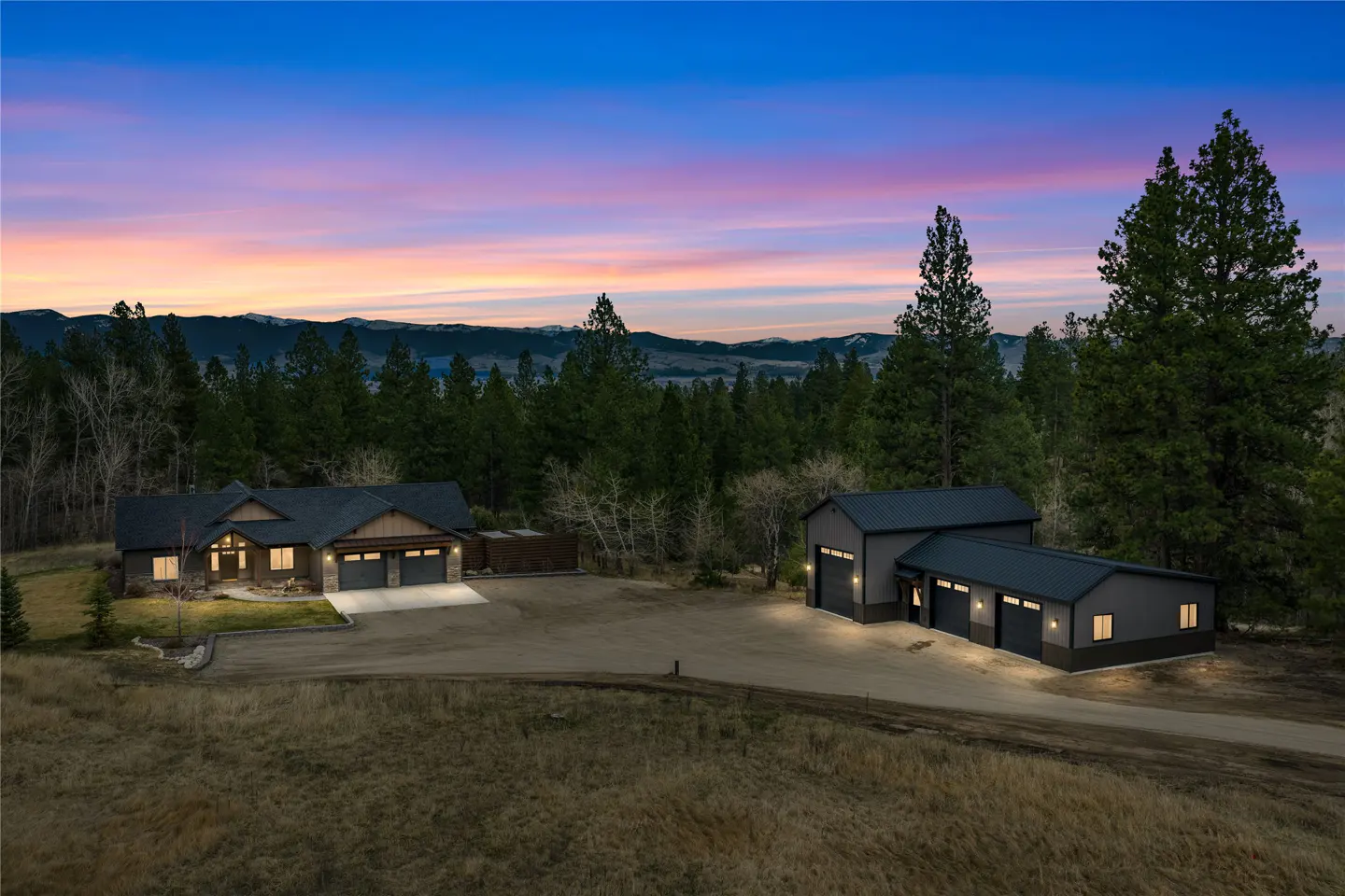 A dusk view of a gray house with a two-car garage and a gray outbuilding with three garage doors.