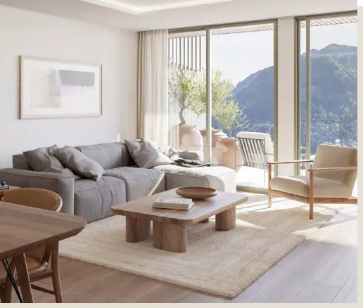 Bright living room with gray sofa, wood table, and beige chair. Large windows offer a mountain view.
