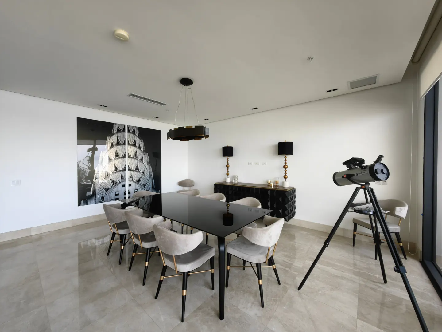 Bright dining room with a black table, gray chairs, and a telescope near a window. A black and white photo hangs on the wall.