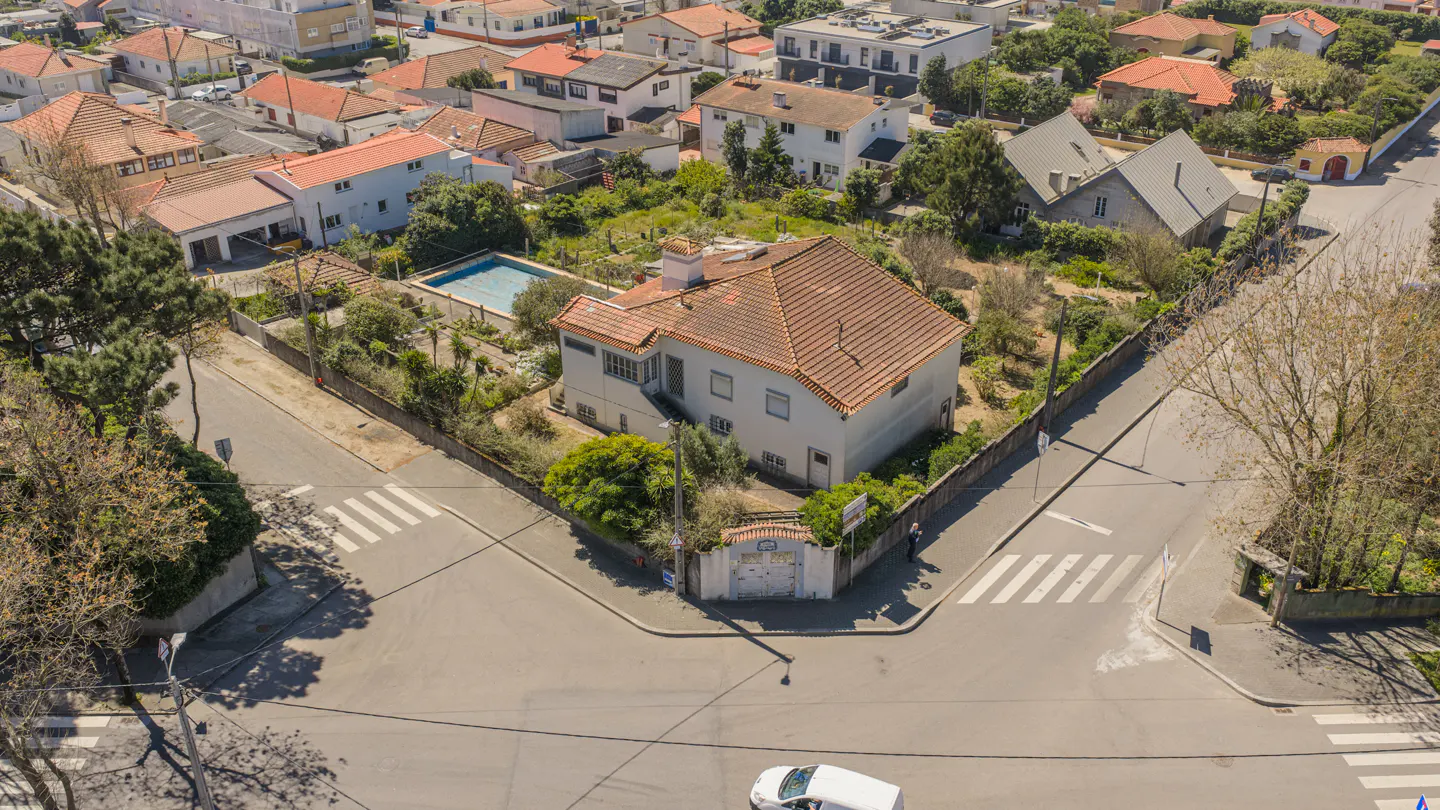 Aerial view of a white two-story house with a red tile roof, a pool, and a white car on the street.