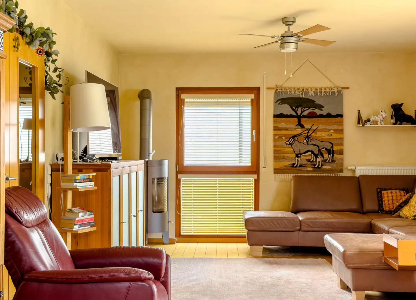 Cozy living room with a red leather armchair, brown sectional sofa, wood stove, and a wall tapestry featuring oryx.
