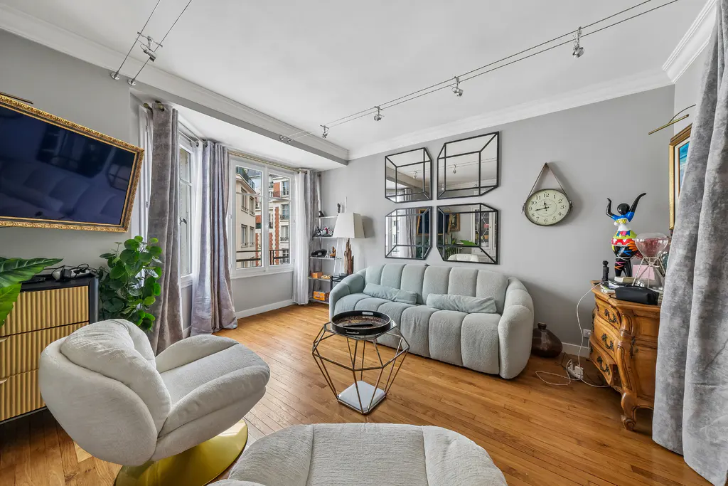 Living room with hardwood floors, gray walls, and track lighting. A light blue sofa sits beneath four square mirrors. A white chair is in the foreground.