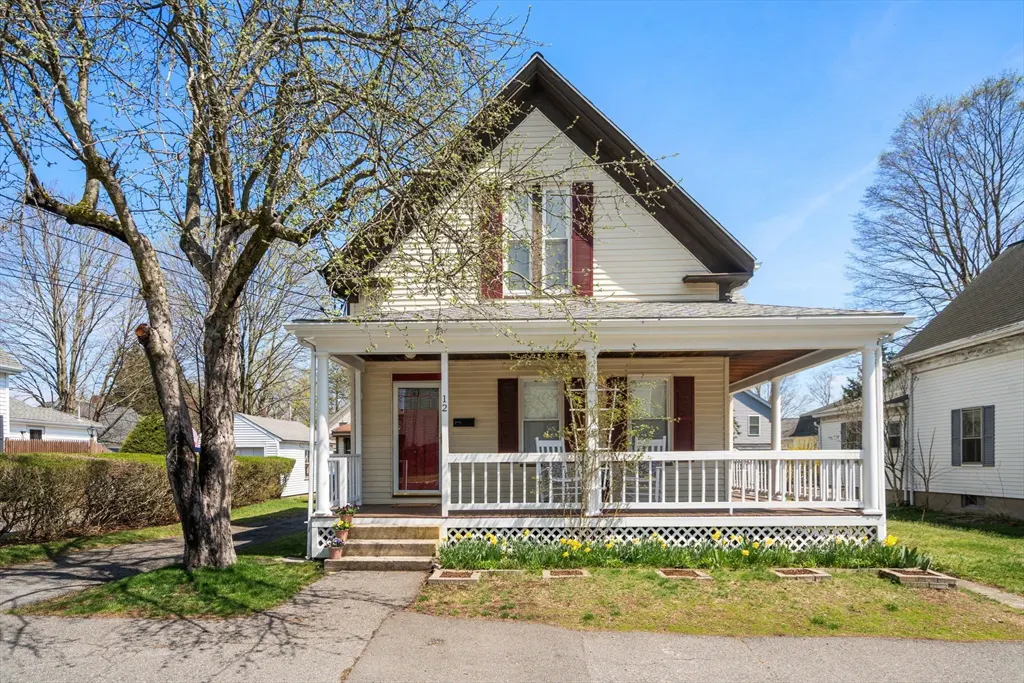 A cream-colored two-story house with a front porch, red door and shutters, and a tree in the yard.