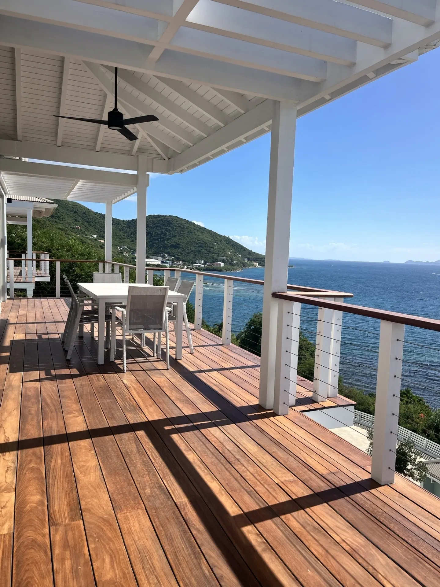Outdoor patio with a wood deck, white table and chairs, and ocean view.