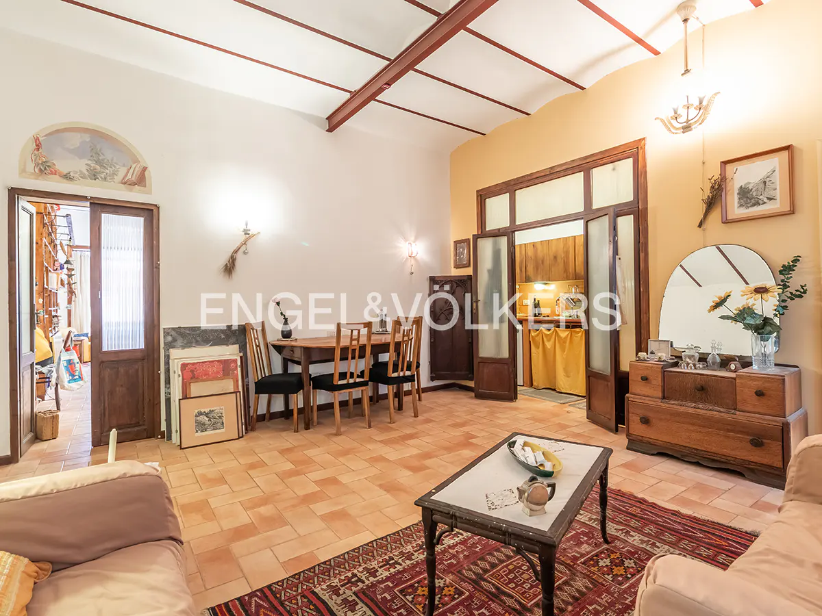 A living room with terracotta tile flooring, a dining table, and a coffee table on a red patterned rug.