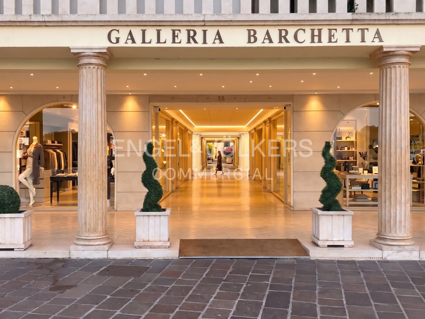 Exterior view of Galleria Barchetta, featuring storefronts, columns, and a person walking through the illuminated hallway.