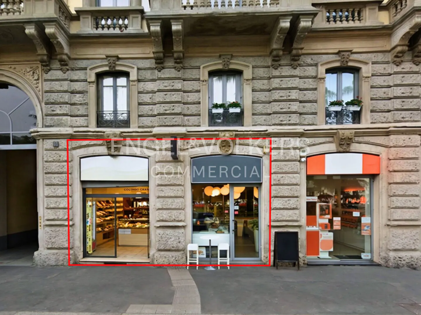 Exterior view of a commercial building with three storefronts, each with large glass windows and stone facade.