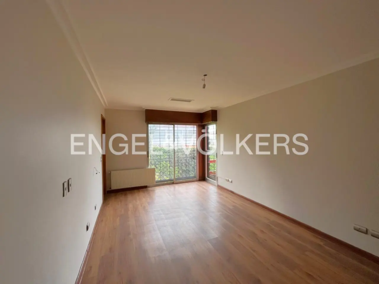 Empty room with hardwood floors, white walls, and a large sliding glass door leading to a balcony. A radiator is under the window.