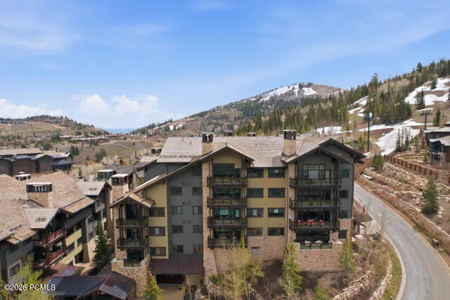 Exterior view of a multi-story condo building with balconies, set against a mountain backdrop under a blue sky.