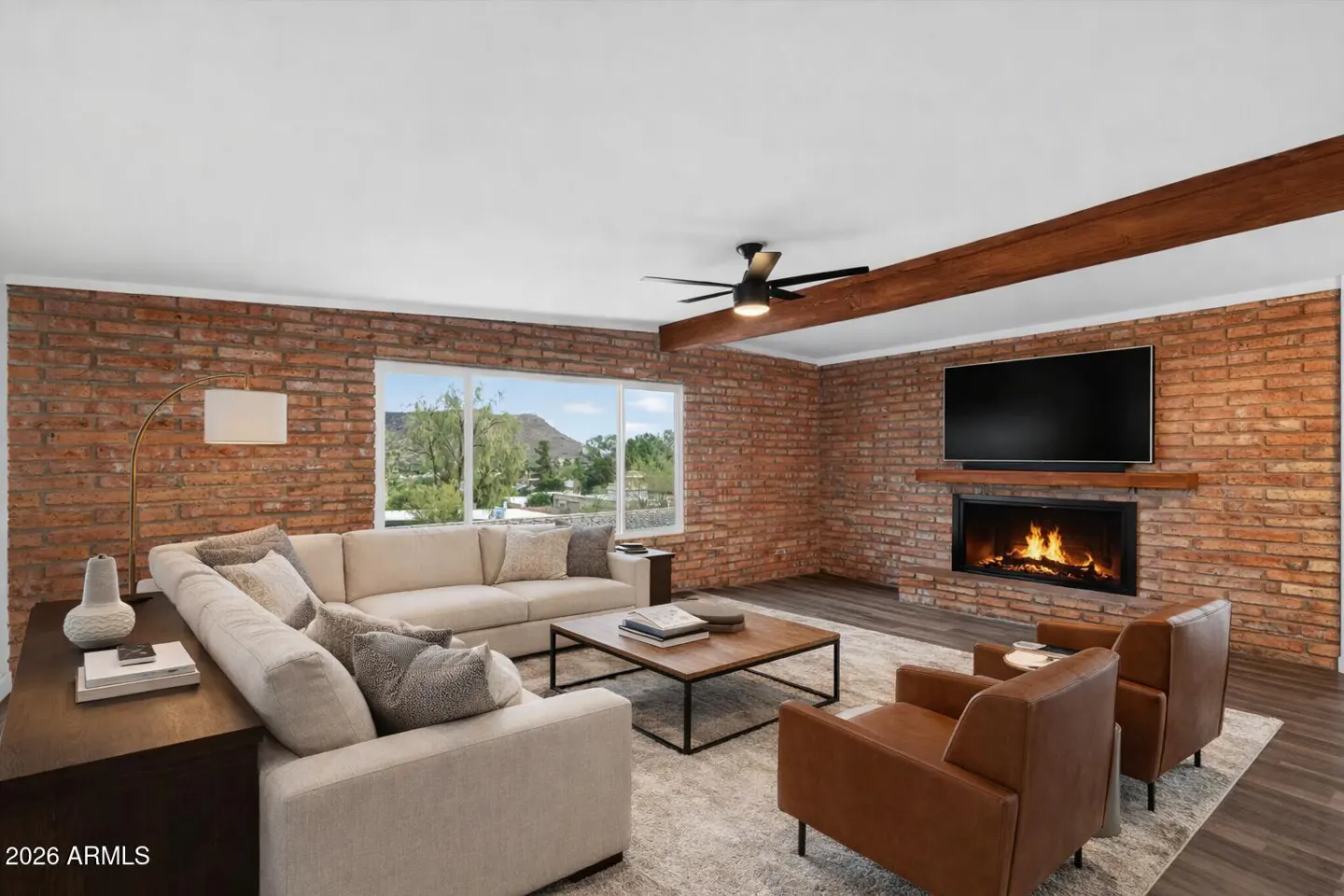 Living room with brick walls, a fireplace with a TV above it, a beige sectional sofa, and two brown leather chairs.