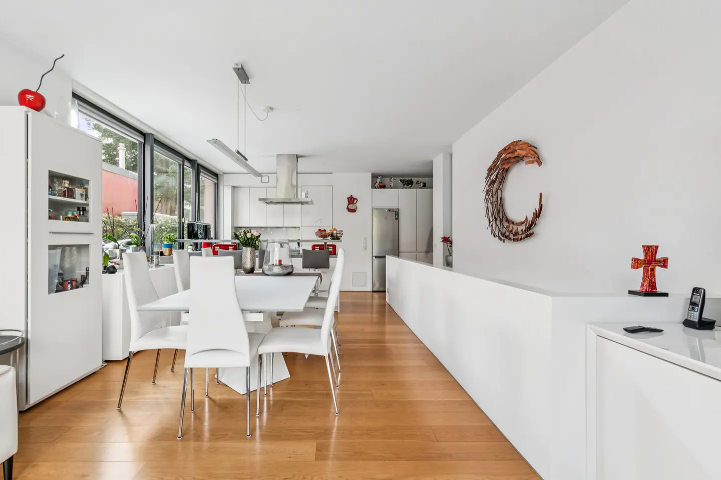 Modern dining area with white chairs, a white table, hardwood floors, and a crescent-shaped wall sculpture.