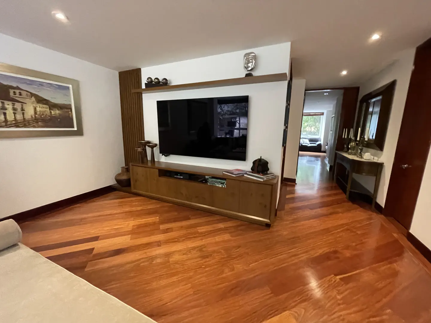 Living room with hardwood floors, a large TV mounted above a wooden cabinet, and a painting on the wall.