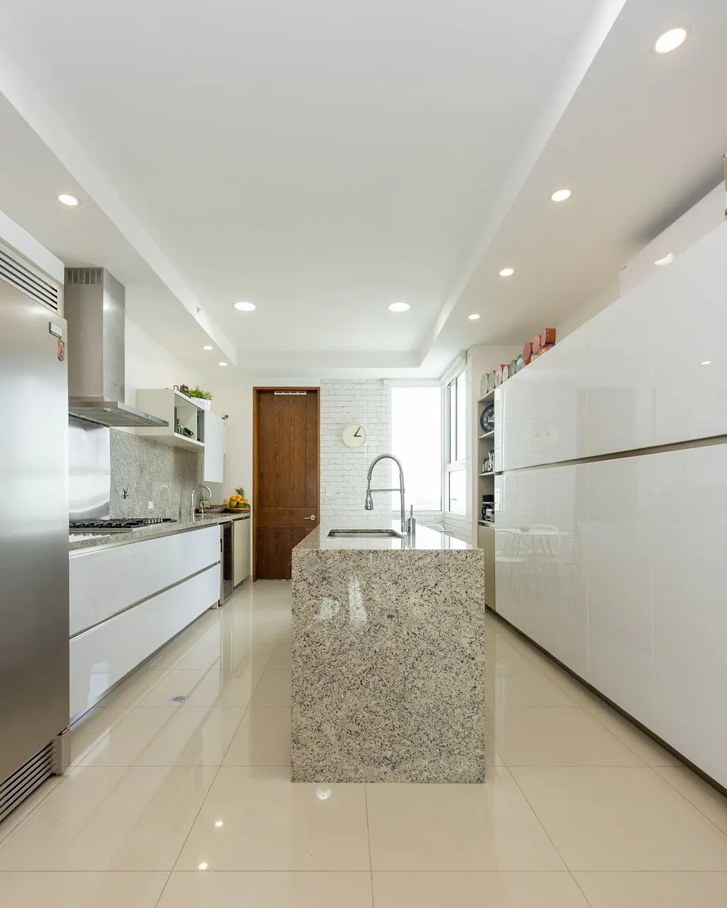 A modern, bright kitchen with a granite island, stainless steel appliances, and white cabinets.