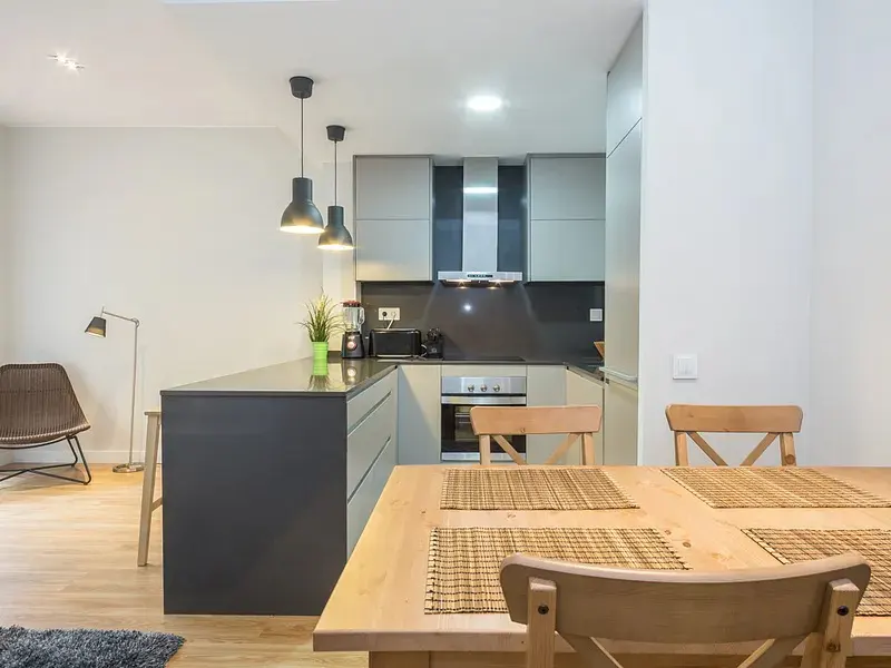 Modern kitchen with a wooden dining table, grey cabinets, stainless steel appliances, and two pendant lights.