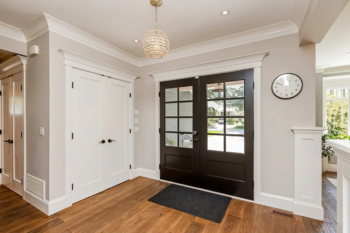 Foyer with hardwood floors, white walls, and dark wood double doors with glass panes. A crystal chandelier hangs from the ceiling.
