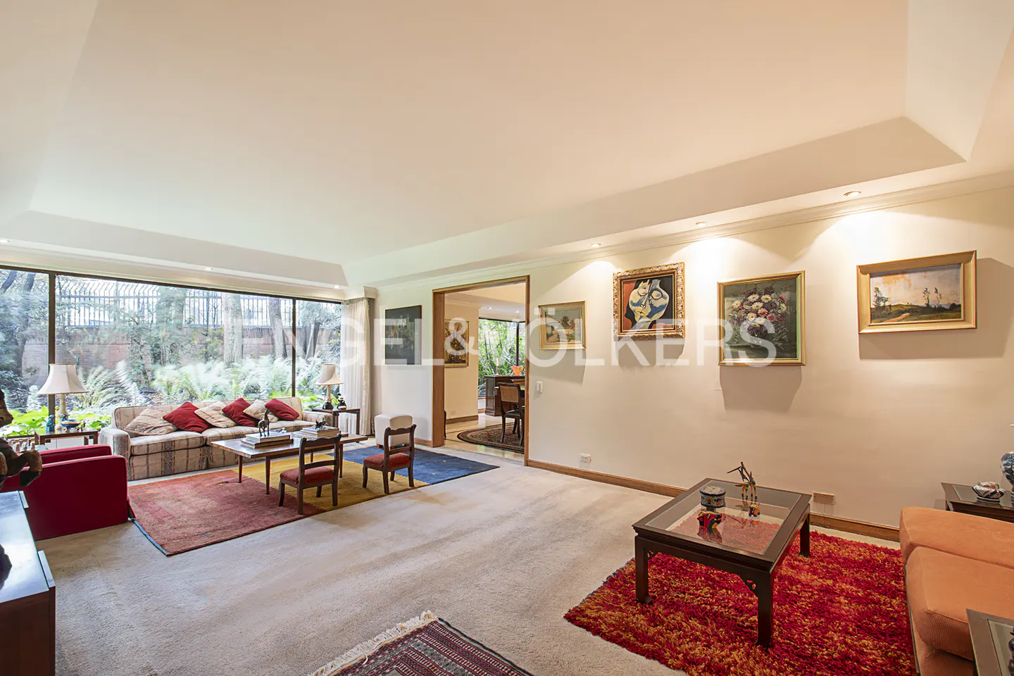 Bright living room with large window, patterned sofa, red accents, and framed art on the wall.