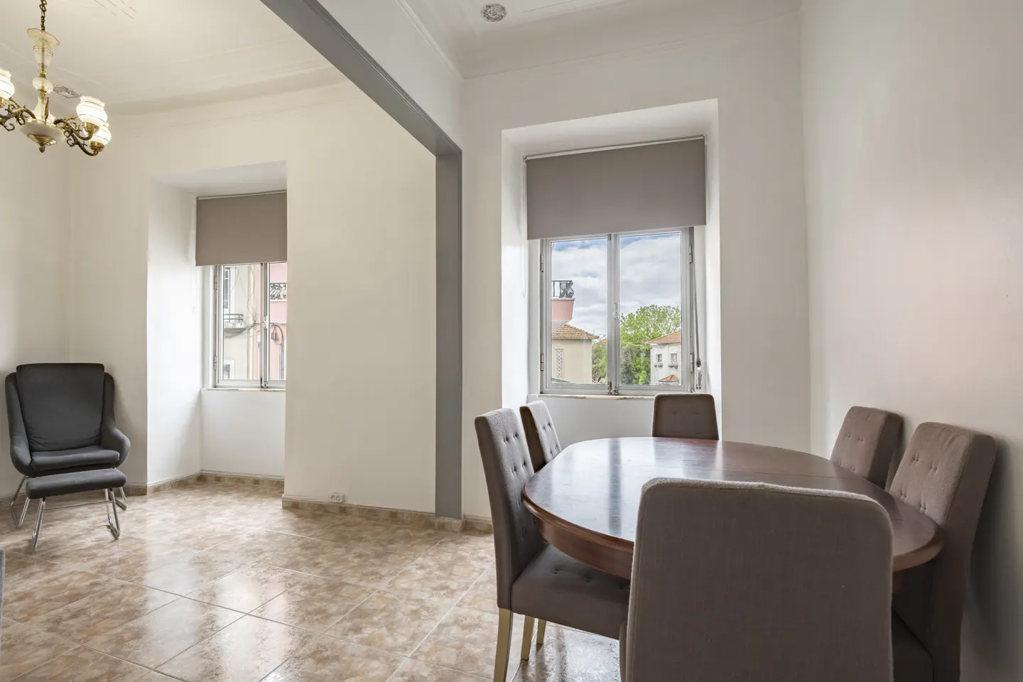 Bright dining room with a dark wood oval table, six brown chairs, and a window with a view of buildings and trees. A gray chair is in the adjacent room.