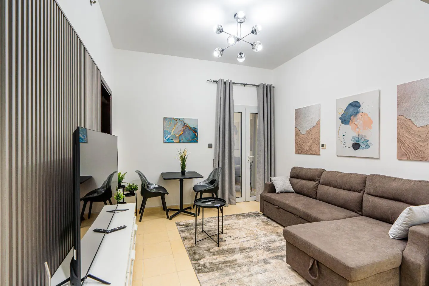 A modern living room with a brown sectional sofa, a small black table with two chairs, and abstract art on the white walls.