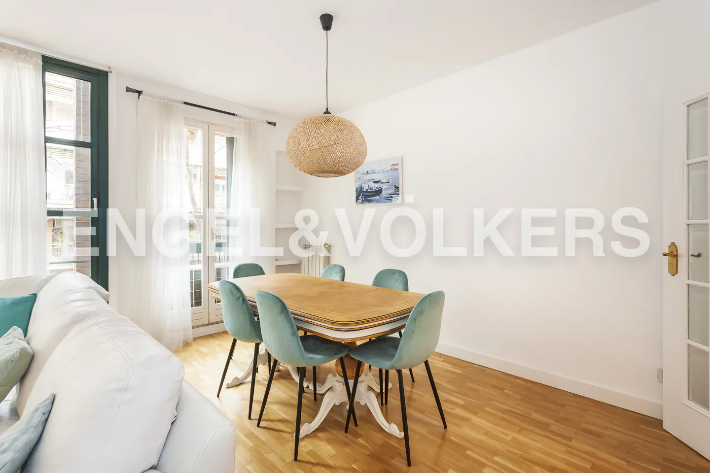 Bright dining area with wood floors, a table with six teal chairs, and a woven pendant light. White sofa and Engel & Volkers logo visible.