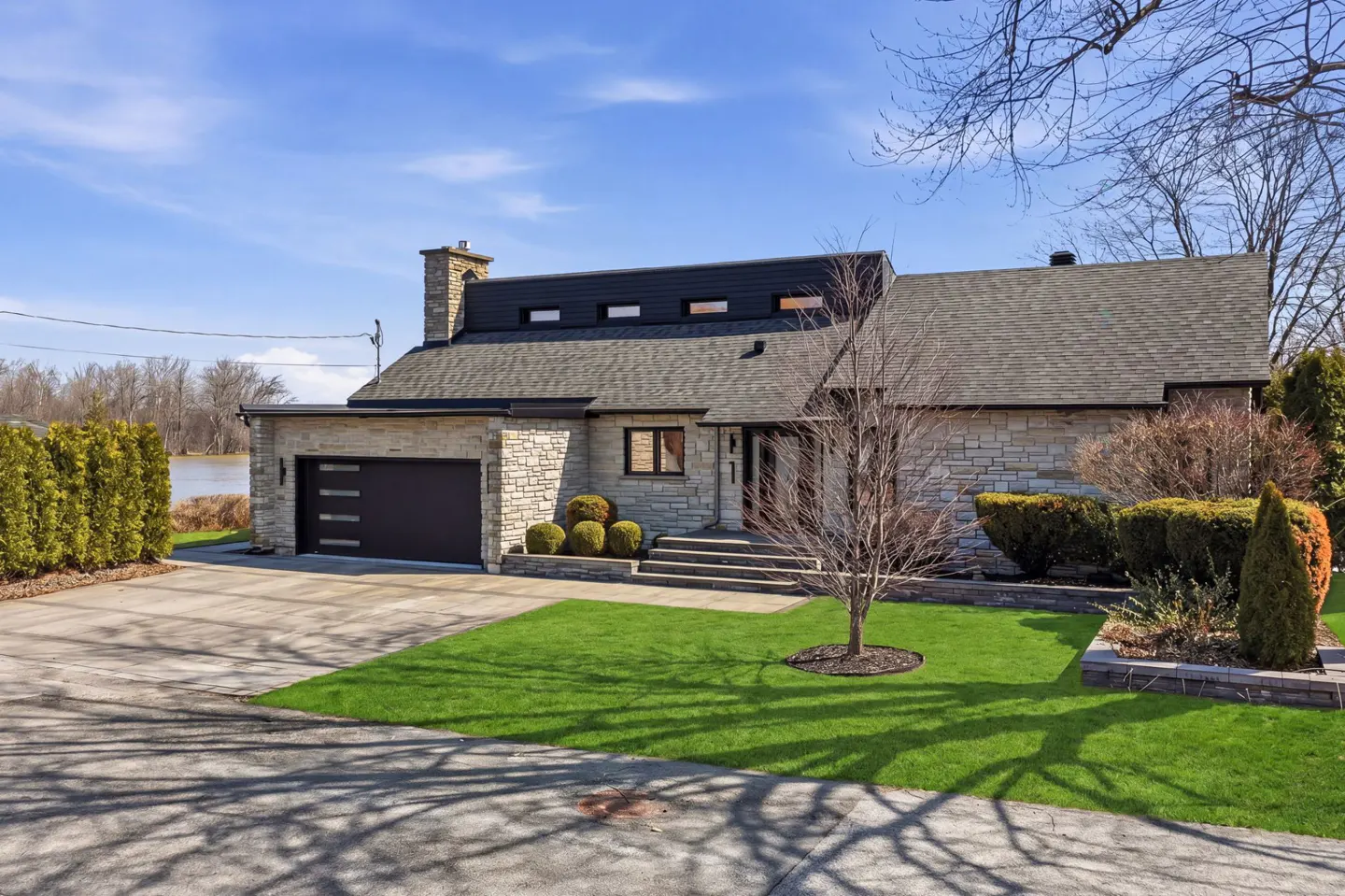 Exterior of a stone house with a black garage door, green lawn, and blue sky.