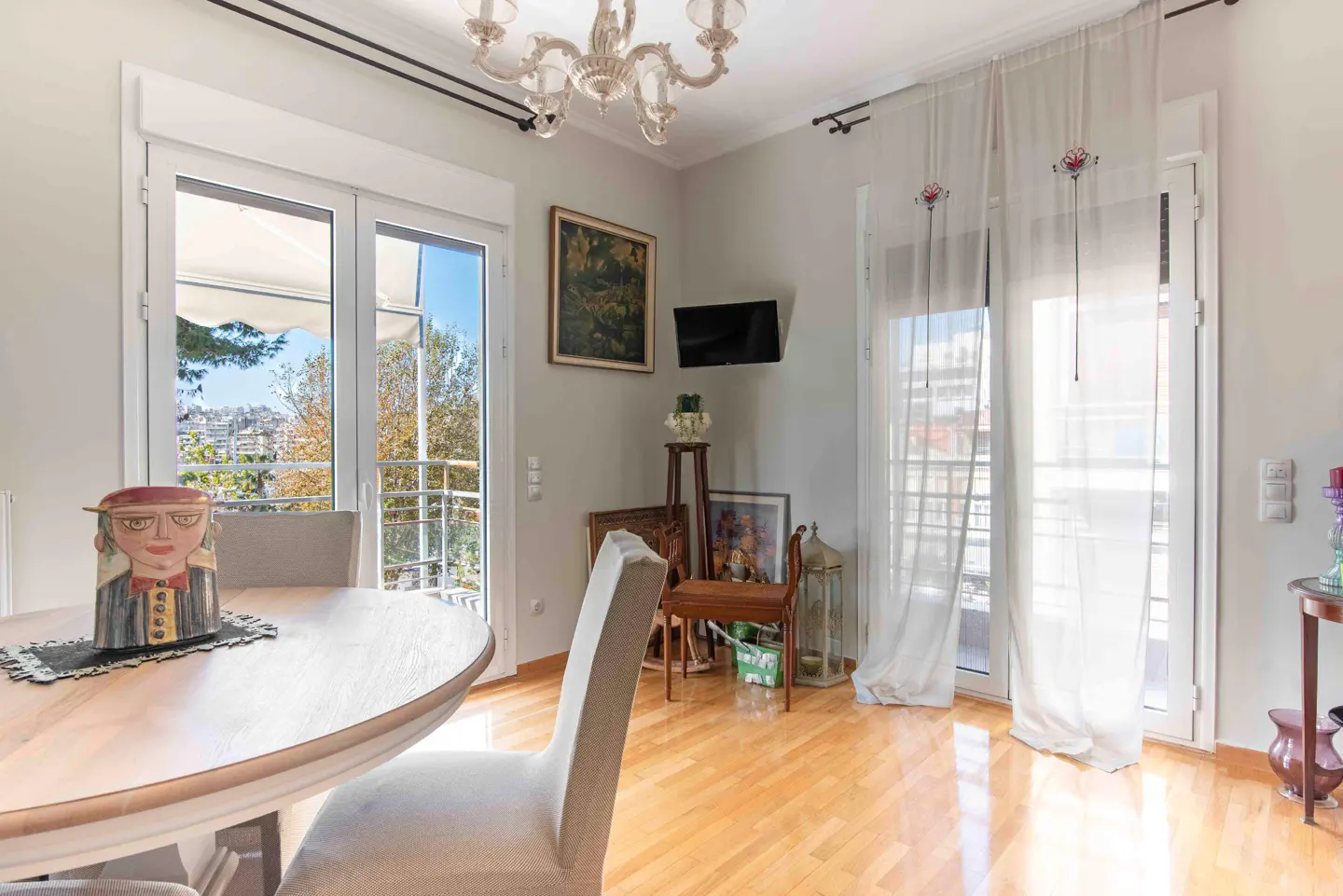 Bright dining room with light wood floors, a round table, chandelier, and glass doors leading to a balcony.