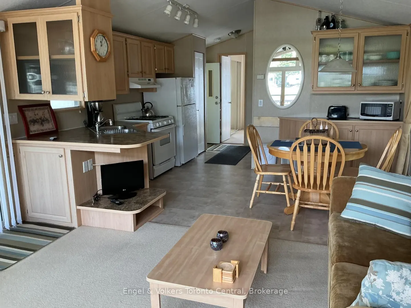 A bright, open-concept kitchen and living area with light wood cabinets, a dining table, and a brown sofa.