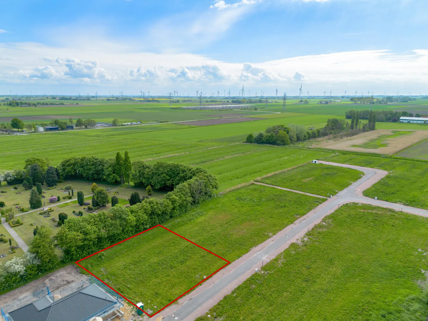Aerial view of a grassy lot outlined in red, with green fields and wind turbines in the background.