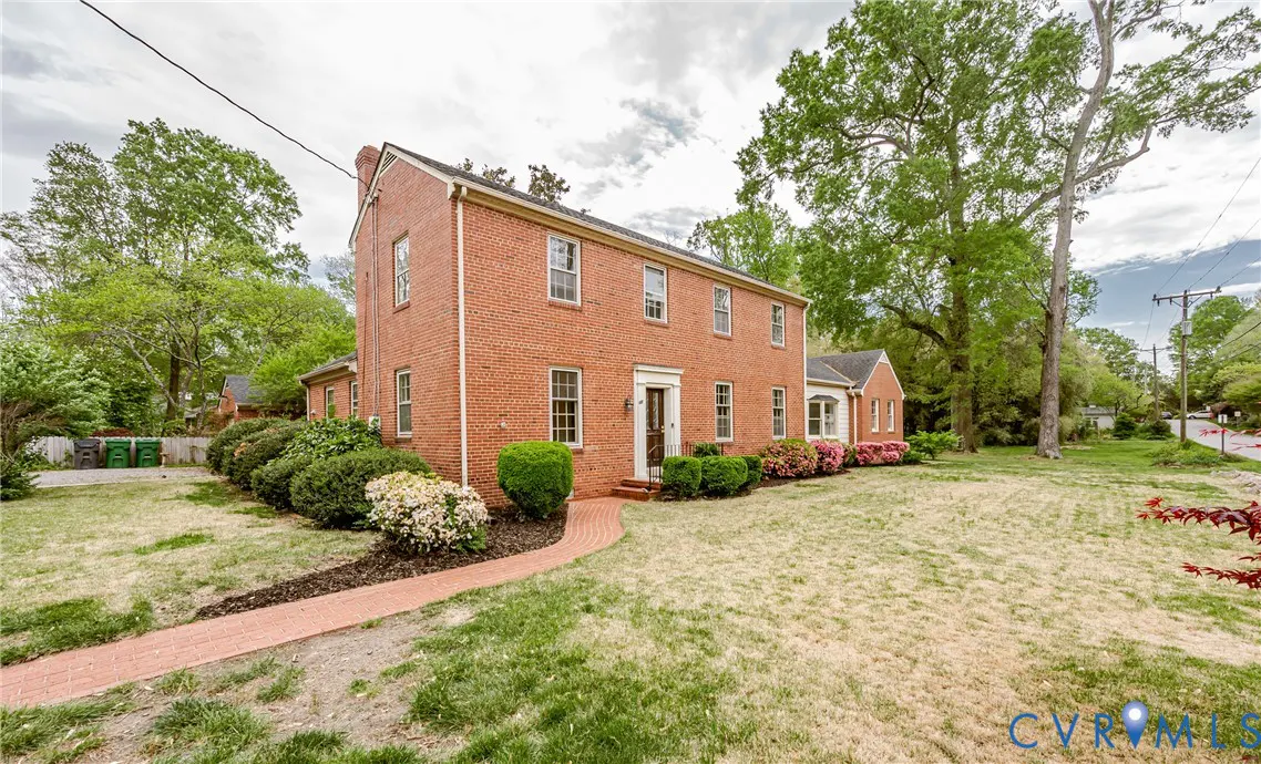 Two-story red brick house with a brick walkway, green lawn, and landscaping.